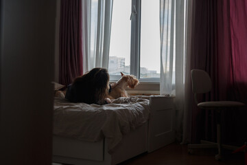 A girl and a dog on a large bed in a room by the window