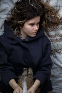 The girl lies on the bed and holds a cat. Portrait