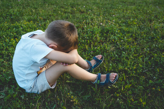 Boy is sitting on the grass and covering face with his hands