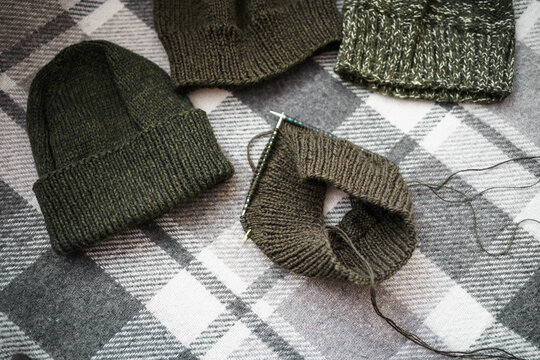 hand-knitted hats of various shades of green on a checkered plaid