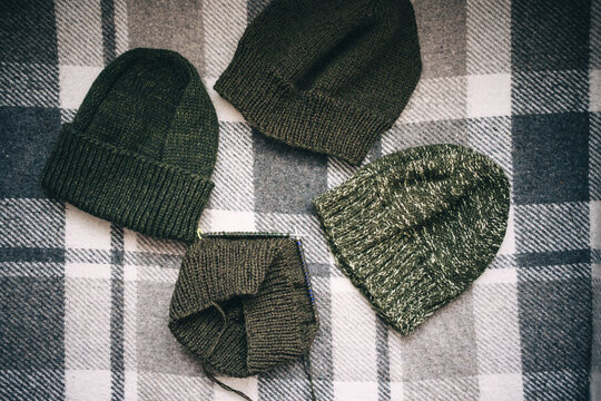 hand-knitted hats of various shades of green on a checkered plaid