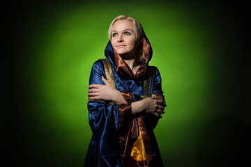 a fortune teller in an old-fashioned dress hugged herself and looks away on a dark green background