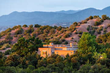 Fototapeta premium Sunset in Santa Fe, New Mexico mountains in Tesuque community neighborhood with sunlight on house home with green plants and shrubs and dark blue sky on high desert
