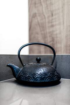 Traditional teapot on table of zen minimalist home with wooden wall background and vertical closeup view of cast iron tea teaware