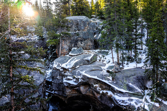 Independence Pass snow covered Rocky Mountain landscape view of sunrise by grottos cave pool rocks near scenic byway in morning near Aspen, Colorado with sun flare sunburst