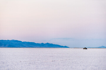 West Wendover, USA car driving on white Bonneville Salt Flats near Salt Lake City, Utah on border of Nevada with purple pastel sunset colors