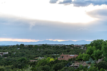 Fototapeta na wymiar Colorful sunset in Santa Fe, New Mexico with green foliage high desert and cityscape buildings adobe houses with mountains silhouette in background