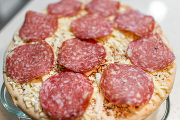 Macro closeup of uncooked raw take and bake frozen pepperoni mozzarella cheese pizza pie on tray ready for baking cooking