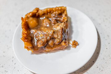 Macro closeup of one cooked piece of pecan pie with dough crust on plate isolated on white background