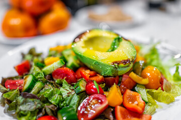 Macro closeup of chopped sliced vegetables on white plate with fresh vegan salad with romaine lettuce salad, tomatoes, bell peppers and avocado half