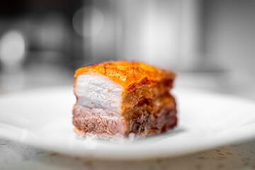 Macro closeup side view of cut fresh barbecue cooked baked fried pork belly fat bacon meat with crispy crunchy skin, nutritious food isolated against white plate at kitchen table