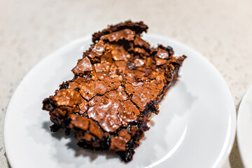 Macro closeup of one homemade baked brownie chocolate cake piece dessert bread, sweet food with crumbles on kitchen table plate on white background
