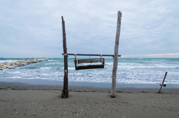 Due pali sorreggono una sedia a dondolo sulla spiaggia di Pellestrina in una giornata d'inverno, cielo, nuvole, 