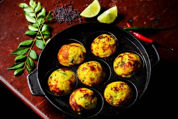 Pan with fried dish in designated small areas on a red marble table with spices and lime slices