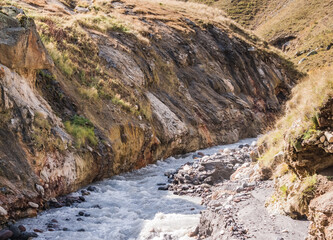Mountain noisy fast river rustles and foams in a rocky gorge with steep banks, sunny autumn day in the mountains
