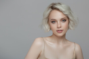 Portrait of a beautiful blonde girl with a short haircut. Gray background.