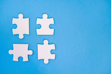 Obraz premium Four whiie jigsaw puzzle pieces on blue background ready to be fitted togther with negative space for copy.