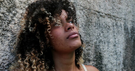 Casual Pensive hispanic woman leaning on wall looking at sky