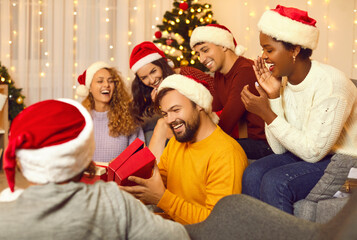 Fototapeta premium Smiling multiracial friends exchange Christmas gifts at celebration at home together. Happy diverse international group of young people greet congratulate with New Year give presents.