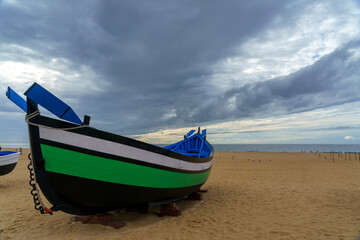 colorful old green fishing boat displayed on a beach with a dramatic cloudy sky and horizon