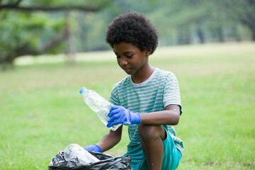 Volunteer kid. African American boy in gloves picking up plastic bottles into a black garbage bag...