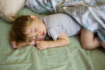 Cute sleeping baby. Children's Daytime sleeping. The Little Caucasian Boy sleeping on stomach in a big bed under a blanket. Close-up portrait of a beautiful sleeping blond child.