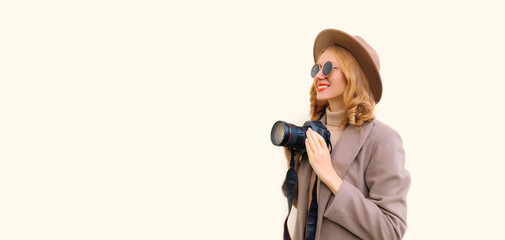 Portrait of stylish happy smiling woman photographer with digital camera taking picture wearing round hat, brown coat on background, blank copy space for advertising text