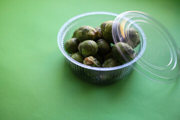 Brussels sprouts juicy green cabbage in a transparent container on a green background with water drops. for shop labels intro banners recipes