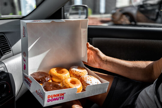 Naples, USA - October 27, 2021: Man holding Half a dozen of Dunkin Donuts doughnuts in carboard container box, glazed deep fried dessert pastry of Boston cream, chocolate filling