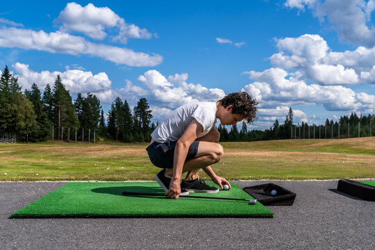 Young adult male golfer sitting in foreground at a golf course driving range preparing the golf ball.