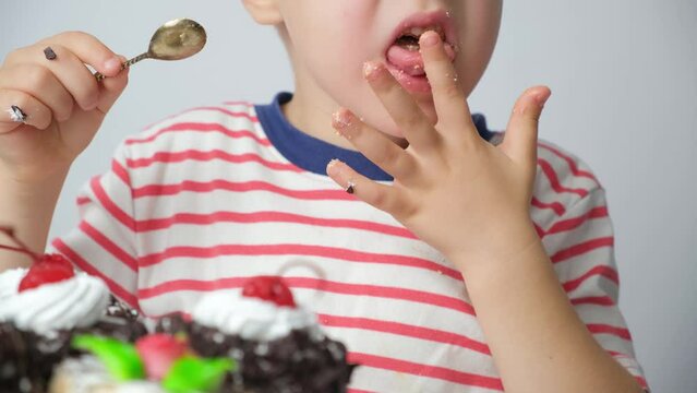 A 5-year-old boy eats cake, licks his fingers and wipes his dirty fingers on his clothes.