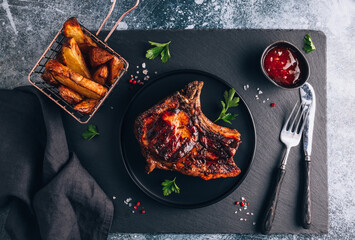Grilled pork steak, baked potato and chili sauce on a dark stone background