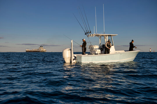 People fishing on a boat with a freighter in the background.