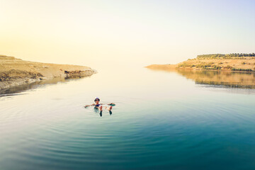 Happy female tourist float on dead sea water happy enjoy vacation in middle east. Sunset panorama with person in salty lake water