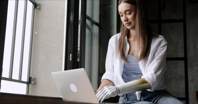 Motivated woman using prosthetic arm working or learning notebook computer, girl with disability typing text artificial prosthetic limb