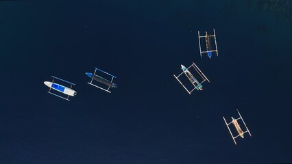 Beautiful aerial top view of white fishing Jukung boats on clear blue ocean water through which the sea reef is visible. ship vessels on sea surface in twilight. Film grain texture Soft focus