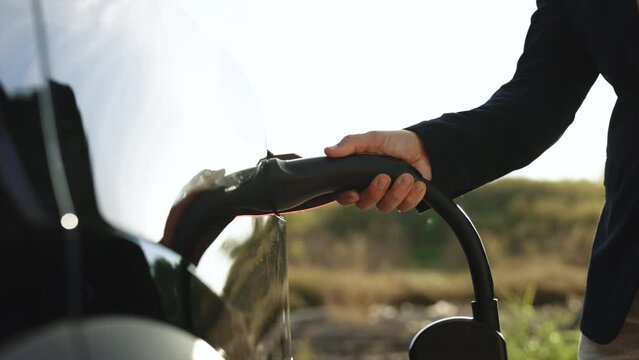 Close up of unrecognizable male hand inserts power connector into EV car uses smartwatch for activates start charging. Businessman plugging in charging chademo cable type 2 europe to electric vehicle