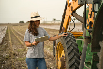 Portret van lachende jonge vrouw boer met behulp van tablet en tractor voor oogst. Moderne landbouw met het concept van technologie en machines