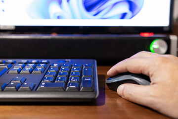 Selective focus on a hand that is clicking on a mouse with monitor and soundbar out of focus in background.