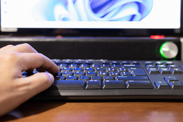 Selective focus on a hand that is typing on a keyboard with monitor and soundbar out of focus in background.