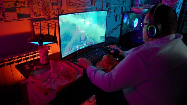 The gamer plays at the computer and eats a burger and pizza. A Thick programmer writes code and eats a burger and pizza.