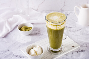 Green matcha ice tea with cream cheese in a glass on the table. Trendy homemade drink.