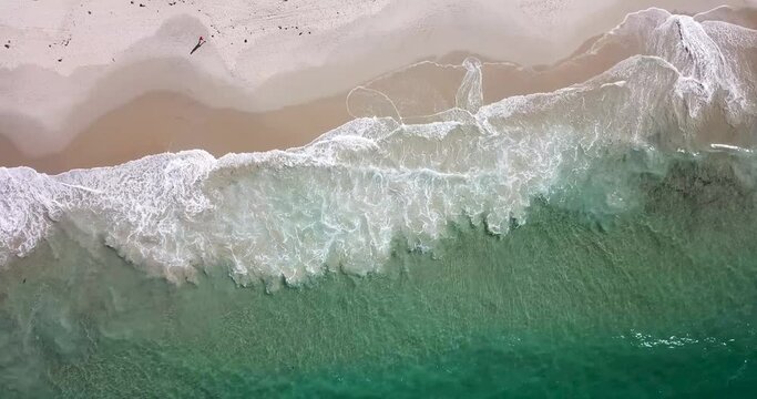 Aerial footage of ocean waves gently breaking along a sandy beach