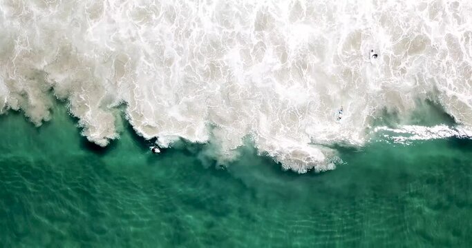 High altitude aerial view over emerald wave undulating and surfers paddling 
