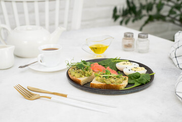 A healthy breakfast with two sandwiches with avocado, boiled egg, salmon, cup of tea on a gray table. Top view.