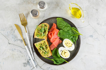 A healthy breakfast with two sandwiches with avocado, boiled egg and salmon on a gray background.