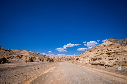 Low Angle Shot Of A Pavemented Road In The Desert With Bushes On The Sides Under The Blue Sky