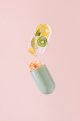 Green transparent pill with lemon, tangerine, kiwi and lime on isolated pastel coral pink background. Minimal pharmaceutical abstract concept of supplements. Natural fruit sources of vitamin C.