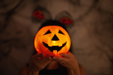 Person wearing halloween costume holding spooky jack-o-lantern glowing in from of the face in the dark decorated party room