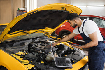 Young mechanic using tablet computer, recording automobile engine checks collect detailed...